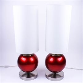Pair of Contemporary Red and Silver Metal Lamps: A pair of contemporary red and silver tone metal table lamps, by Anthony California Inc. The matching pair of lamps feature round, brushed chrome finished bases with round, glossy apple red columns. They are topped with tall, tubular white fabric shades. A maker’s label is affixed to the undersides.
