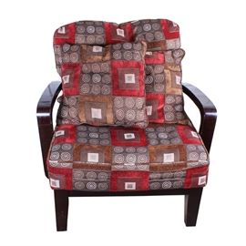 Contemporary Armchair: A contemporary armchair. The chair features dark stained wood arms, with square straight legs. The chair has a box seat cushion and a large back pillow, plus two matching throw pillows. The chair and pillows are upholstered in a print featuring brown and red squares, with alternating squares that have white pinwheels. No maker’s marks. Located on an upper floor.