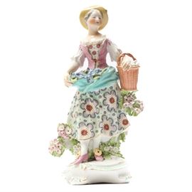 18th Century Derby Porcelain Figurine: A Darby porcelain figurine circa 1770’s. This winsome lady is an early Darby figurine who has been painstakingly modeled, hand painted and incredibly detailed. This piece captures the ideal English lady going about her daily duties of collecting fresh eggs and gathering flowers in a jaunty hat, bright gown and highly ornate shoes. Flowers adorn not only the dress, but seem to bloom wherever this lady appears including the white base with scrolled legs upon which she stands. Unmarked.