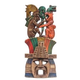 Carved Mayan Warrior Mask: A Mayan wooden warrior mask. Carved from tropical wood, this piece features a warrior in an intense battle against a jaguar and a large snake. The warrior is seated upon red and green shapes lined with gold and shows worry to his expressive face. A pyramid temple is settled in the center of the mask, above an opened mouth warrior face with flanking adornments. The mask hangs with a wire to verso. This item matches 17COL081-085 in this sale.