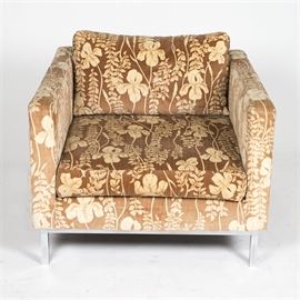 Mid Century Modern Upholstered Armchair: A Mid Century Modern armchair. This piece features a straight crest rail and high armrests with a cushioned back and seat rising on a metal frame. It is upholstered in a brown and cream fabric with repeating iris patterns throughout. The piece is marked with a tag that reads “Trenton House Upholstering, Riverview, Michigan” below the seat cushion.