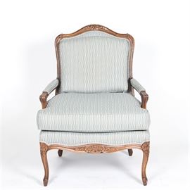 Vintage Louis XV Style Upholstered Fauteuil: A vintage Louis XV style upholstered fauteuil. This piece features a wood frame and a carved, curved crest rail with upholstered back and arm pads on curved supports flanking a button tufted cushion seat above an apron featuring floral carved detail rising on decorative cabriole legs. This piece is upholstered in a blue fabric with colorful flecks. There are no visible maker’s marks or labels on this piece.