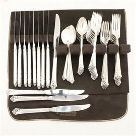 Oneida Heirloom "Damask Rose" Sterling Flatware: A sterling silver flatware set by Oneida. These are in the Damask Rose pattern featuring narrow stems that flare to triangular handles ornamented with rose blossoms. This set includes dinner forks, salad forks, teaspoons, and dinner knives with stainless steel blades and hollow handle. They are marked “Heirloom Sterling by Oneida”, and are presented within a silver cloth case.