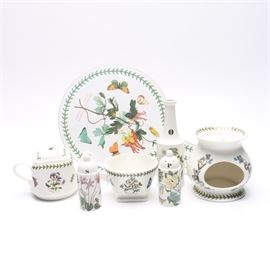 Portmeiron "Botanic Garden" Ceramic Tableware: A collection of Portmeiron Botanic Garden tableware. This collection includes a chopping board, a teapot, a bowl, salt and pepper shakers, an oil bottle and a tart warmer candle holder, all in white with labeled illustrations of flowers and plants. These pieces are marked, “Botanic Garden designed by Susan Williams-Ellis Portmeiron® dishwasher, microwave, freezer safe, oven to table”.