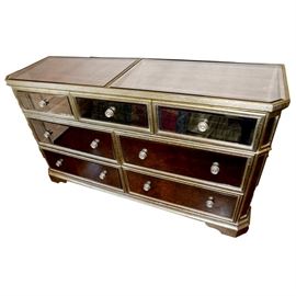Hollywood Regency-Style Mirrored Dresser: A Hollywood Regency-style mirrored dresser. This dresser has a wooden antiqued finished frame mounted with a beveled mirrored surface and exterior. It is complete with three small top drawers and four larger bottom drawers.