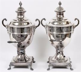Lot#1002, HARROD'S OF LONDON SILVER PLATED TEA URNS, PAIR, H 23", W 13"The urn-form body with molded reeded banding, arched acanthus-mounted handles, lion’s head spout with waisted collar, the fitted and domed lid with flame finial, the whole above a square pedestal base raised on four lion’s paw feet en suite. Each stamped with maker's marks to underside.

Provenance: John W. Elkins & Co., November 2000.