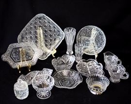 Fourteen Piece Assorted Vintage Cut Glassware: 4.5" W x 2.5" H bowl w/ silver base, 9.5" W x 9.5" D x 1.5"H square dish, 5.5" W x 9" D rectangular dish w/ handles, 8" W x 4" D x 1.5" H elongated dish, 4" W x 6.25" D x 2" H oval dish, 6.25" W x 1.5" D scalloped edge dish, 6" W x 1" H dish w/ sawtoothed edge and handle, 3" W x 4" D x 3" H jam dish w/ lid, 4" W x 3.25" H fluted dish, 7.25" W x 1.5" H divided circular dish, cream & sugar set, 2" W x 4.75" H vase, 3" W x 8" H vase
