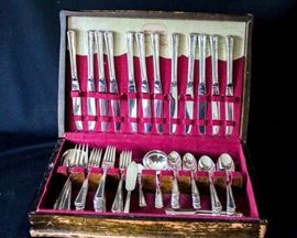 Twelve Piece Place Setting: Inlaid silver plate made by International Silver Co. Twelve five piece place settings, four large serving spoons, one large meat fork, butter knife, soup ladle, sugar spoon, eight place setting butter knives. Set includes wood silver box in used condition with one broken hinge.