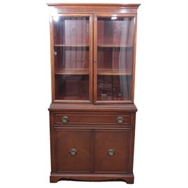 Vintage Hepplewhite Wooden China Cabinet: A vintage Hepplewhite china cabinet. Features glass doors over single drawer and double blind under cabinets. Inside lower cabinet there is one fixed shelf. Inside the main cabinet are two fixed shelves with plate groves. Hepplewhite pulls and hardware have a bronze patina. This piece finishes upon ogee bracket feet.