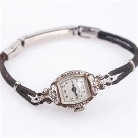 Bulova 14K White Gold and Diamond Watch: A vintage Bulova 14K white gold and diamond wristwatch. The watch features a 14K white gold case with gold filled hardware on a braided black cord. The watch is decorated in an ornate Edwardian style case and is embellished with diamonds. The timepiece bears the number "36365” stamped to the verso.