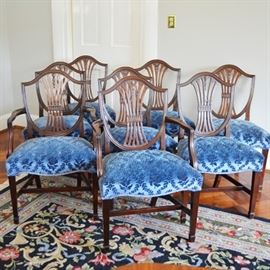 Antique Hepplewhite Dining Chair Set By Schmieg & Kotzian: The set of eight antique Hepplewhite mahogany dining chairs, thought to be constructed by Schmieg & Kotzian. Chairs feature a shield-back design, with a rounded lower edge, a four ribbed splat with bell flower carving, tapered legs and spade feet. The seats are finished with the original blue mohair upholstery in a lattice and floral design. This set includes six side chairs and two armchairs. The chairs include an S mark, and are thought to be by renowned cabinet makers Schmieg & Kotzian, English craftsman who came to US in 1897.