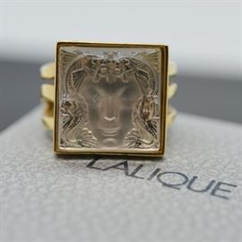 Lalique 10K Gold Plate Crystal Ring: A Lalique 10K gold plate crystal ring. This Art Deco style Masque de Femme motif ring is a square carved crystal. It is designed with the face of a mysterious woman and detailed with an ocean life surround. The crystal is bezel set in a wavy three shank design.