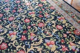 Handwoven French Horn Wool Area Rug: A handwoven French Horn wool area rug. Designed with a french horn and floral motif, this pile rug features an all over design with three floral borders. It includes tones of green, crimson, camel, lavender, and blue against a black field. It also includes handwoven fringe on two ends and was purchased from Aria’s Oriental Rugs, Cincinnati, Ohio.