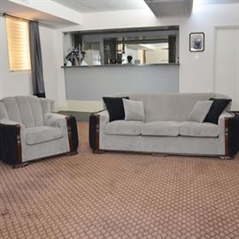 Vintage Art Deco Three Seat Sofa and Chair Set: A vintage Art Deco sofa and armchair set, circa 1930s-40s. This set features black upholstered curved channel arm panels and mahogany wood detailing, and has been reupholstered with a gray plush style fabric. The three seat sofa includes removable seat cushions, with two black accent pillows and two matching gray accent pillows. The chair back features a channel style back design, with a removable seat cushion.