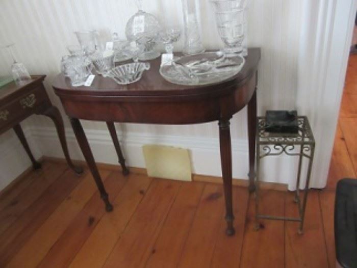 Mahongony game table. One leg opens to support table when opened.  Pressed and patterned glass on top. The brass plant stand on the right has a marble ash tray on top. 