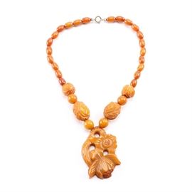 Bakelite Beaded and Carved Necklace: A Bakelite beaded and carved necklace. This orange and amber-colored necklace features various sized carved and smooth beads with a drop Bakelite floral pendant. The piece also includes a silver tone spring ring clasp. No visible hallmarks.