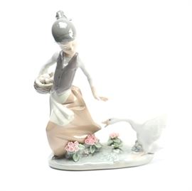Lladro "Girl and Aggressive Goose" Figurine: A Lladro “Girl and Aggressive Goose” figurine. The piece is composed of porcelain in a cool palette of gray, cream, and taupe. It depicts a girl holding a basket and a goose biting at her skirt. It is marked to the bottom Lladro.