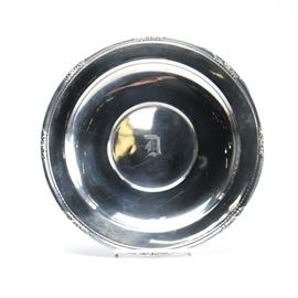 Ellmore Silver Co. Sterling Silver Plate: An Ellmore Silver Co. sterling silver plate. This piece features a round shape with repoussé scrolls around the rim and an engraved “D” to the center in a Gothic font. It is stamped with the Ellmore Silver Co. maker’s mark above “Sterling 461” to the underside. The approximate weight is 7.880 ozt.