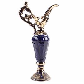 22kt Gold Finished Cobalt Blue Ceramic Pitcher: A 22kt finished ceramic cobalt blue pitcher. This decorative pitcher features a 22kt gold finished serpentine handle and elongated spout with a tapered cobalt blue body and circular gold finished base. The underside is marked “Warranted 22k gold”.
