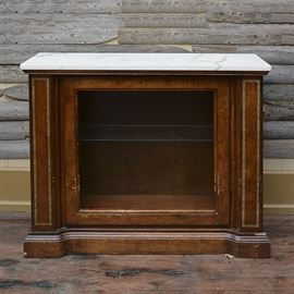 Vintage Console Cabinet With Marble Top: A vintage console cabinet with marble top. This rectangular top cabinet features a white marble top over a full length cabinet door with open panel and an interior glass shelf with a recessed light. This piece sits on a plinth base joining two pilasters with gold tone trim. There are no visible maker’s marks.