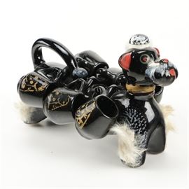 Japanese Black Ceramic Dog Tea Set: A Japanese black ceramic dog tea set. The set features a ceramic dog that holds liquids on the interior and is a holder for six cups on its exterior. Other features include six coffee cups that are black with a curved handle and fluted body with a gilded design. The dog is labeled to the underside “Japan”.