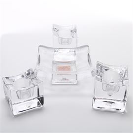 Orrefors Sweden Candle Holders and Kosta Boda "Dad" Domino Holder: A collection of three glass candle holders and a domino holder. This assortment features three square translucent glass candle holders labeled “Orrefors Sweden” and a square art glass domino holder by Kosta Boda marked “Dad” to the center. The candle holders are designed for single candlesticks, and vary in size.