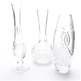 Waterford Crystal Vases: A collection of three vases including Waterford crystal. This collection includes a Waterford crystal beaker vase with a quilted bottom, a narrow lead crystal wedding bud vase, and a narrow Waterford crystal pedestal bud vase with a starburst bottom. Each piece is marked with a trademark or tag.