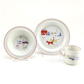 Arabia of Finland Children's Three Piece Place Setting: A Children’s three piece place setting by Arabia of Finland. This group includes a salad plate, a rimmed bowl, and a mug. These pieces feature a matching pattern with depictions of figures, animals, buildings, and automobiles. There are red bands around the edges. The underside of each is stamped “Arabia, Made in Finland”.