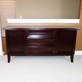 Dark, Contemporary Sideboard by Brownstone Bancroft: A Contemporary style Brownstone Furniture Bancroft sideboard. Constructed of solid hard wood with a deep black cherry finish, it has a simple rectangular shape on short block legs. This sideboard features beveled panel fronts with three center drawers, flanked on each side by a cabinet with three adjustable shelves. 
Companion to 17CIN323-001.