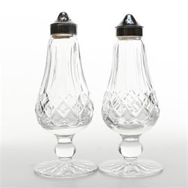 Waterford "Lismore" Crystal Condiment Shakers: A pair of Waterford crystal condiment shakers. Featured are a matching pair of crystal shakers, displaying the crossed cut pattern Lismore. The shakers have silver tone lids and a round pedestal base. Both pieces are marked to the verso.