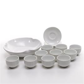 White Ceramics Including Pillivuyt: An assortment of white ceramic tablewares. This approximately fifteen-piece assortment includes four Pillivuyt saucers, ten handle-less coffee cups, and a serving bowl. The cups are fluted on the exterior; they are unmarked. The serving bowl features a pinched rim; it is unmarked.