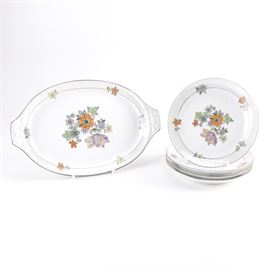 Z. S. and Co. Porcelain Plates and Platter: A collection of porcelain plates and a platter by Z.S. & Co., produced in Germany. This five piece collection includes a platter and four plates. The pieces are white and have colorful printed designs of a variety of flowers, and a silver tone accented rim. The pieces are stamped to their undersides “Z. S. & Co. Bavaria”.