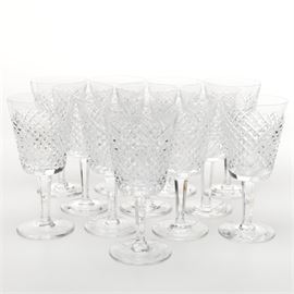 Waterford Crystal Water Goblets: A set of twelve Waterford crystal water goblets. These goblets have flared cylindrical bowls with a diamond grid pattern, faceted stems, and round bases. The bases are marked “Waterford”.