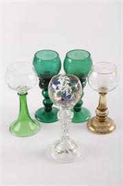 Colored and Painted Glass Stemware: A colored and painted glass stemware assortment. The five pieces in this lot feature a goblet with painted colorful flowers, a turned stem and painted flared foot; a goblet with a clear glass bowl etched with vines and a turned green glass stem that flows outward to the base; a goblet with a clear glass bowl etched with grape vines and featuring a gilt-accented rim, stem and flared foot; and two solid green tinted knobbed stem goblets. These pieces do not present maker or manufacturer marks.