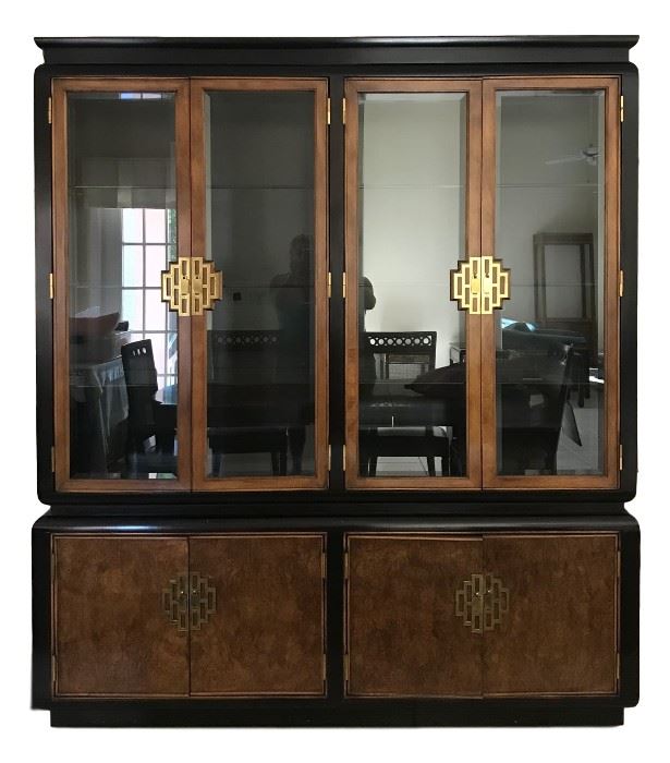 It is a very fine vintage 1970’s Asian style dining room breakfront china cabinet in the Chin Hua Collection designed by Raymond K Sobota and sold through Century Furniture. Large and heavy two piece design with an upper section having a burled elm and ebony lacquered case with beveled glass sides and four glass front doors opening to a black lighted interior with adjustable glass shelves. Lower section having four cabinet doors.
