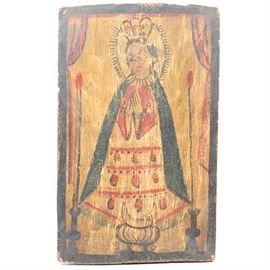Retablo Depicting Nuestra Senora de San Juan de los Lagos: An early 19th Century Spanish Colonial retablo image on board depicting Nuestra Senora de San Juan de los Lagos (Our Lady of San Juan de los Lagos). The image shows Mary in a white and red dress and blue robe holding her hands in prayer. She is standing behind a crescent moon on a pedestal and flanked by two tall candles and framed by red drapes. The image is bordered by a black line. The image is notated with the letters “S” and “O” around the base of the urn. The rustic painting is executed in black, red blue and yellow on a rough hewn board. 1938.0544