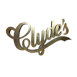 Clyde's Restaurant Sign: A building sign for the historic DC area restaurant group, Clyde’s. This metal sign is gold tone in color with black edges and features the Clyde’s name in its signature font. Metal posts to the back of the sign allow for attaching the sign to a building.