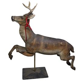 Gustav Dentzel Hand-Carved Reindeer Sculpture: An early 20th century hand-carved Dentzel reindeer sculpture in its original finish. This piece was made by German carousel builder Gustav Dentzel who started the American company, the Dentzel Carousel Company in 1867. This piece is carved from wood and depicts a reindeer mid-gallop. The sculpture features glass eyes, real eight-point antlers, and hand-painted details on the face and ears. A fabric harness is attached to the face and a red rope with bells is hanging off the ear. The reindeer is mounted on a black metal pole attached to a rectangular base.