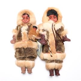 Carlson Dolls Company "Inuit, The People" Dolls: A pair of Carlson Dolls Company “Inuit, The People” dolls. Both the dolls have black hair and dark hand-painted skin and features with sleep eyes. Each is adorned with furred coats and pants and faux leather mittens and boots. One holds a small baby in their arm, and has a tag reading “Inuit The People, Made in U.S.A. for Arctic Circle Enterprises” on the arm.