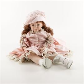 Diana Effner Porcelain Doll: A Diana Effner porcelain doll. This doll has a pale pink bonnet, red curly hair, a floral long sleeve and pink petticoat style dress, lace trimmed socks and strap shoes with a bow. There is a marking to her neck which says “Diana Effner and Ganny Ciss 1995”.