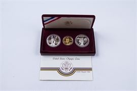 1984 Olympics Ten Dollar Gold Coin, with Related Silver Coinage: A 1984 Olympics ten dollar gold coin, with 1983 and 1984 Olympic silver dollars. Metal Content: 90% gold, 10% copper and 90% silver, 10% copper, respectively. Diameter: 27 mm and 38.10 mm, respectively. Weight: approx. 16.718 grams and 26.73 grams, respectively. Very good condition. See 17CIN316-022.