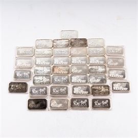Large Grouping of Silver Towne One Troy Ounce .999 Silver Ingots: A large grouping of approximately 39 Silver Towne one troy ounce .999 silver ingots. The obverse of each rectangular bar features a relief image of a horse drawn vehicle or a mining camp in Nevada. The reverse features “One Ounce .999 Fine Silver” and “Silver Towne Winchester, Indiana”. Some come in a protective plastic sleeve. See also 17CIN316-065.