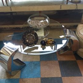 Polished chrome and Kidney shaped glass coffee table with signed Murano cowboy laying down, large glass bowl and a decorative VW auto part.