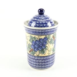 Boleslawiec Pottery Ceramic Urn: A Boleslawiec Pottery ceramic urn. The piece is blue and white in color with a pattern along the exterior that depicts grapes and vines n a palette of dark green and off white. The jar is topped with a matching lid that is topped with a knob finial. The jar is marked to the underside “Boleslawiec, Handmade in Poland”.