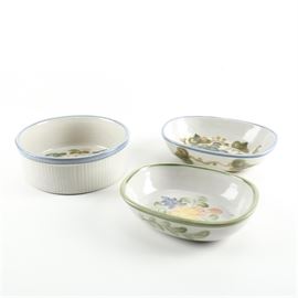 Louisville Stoneware Bowls: A selection of Louisville Stoneware bowls. This selection includes an oval bowl with a painted grape bunch design, a squared bowl with rounded corners and a painted floral design, and a round casserole dish with a painted floral design. Each piece is marked “Louisville Stoneware Made In Kentucky” to the base.