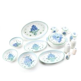 M. A. Hadley Pottery Tableware: A set of M. A. Hadley pottery tableware. The fourteen vintage pieces in this lot include one lidded casserole dish; two medium bowls; one large bowl; two pairs of salt and pepper shakers, one pair larger than the other; two medium oval serving dishes; one large oval serving dish, two lidded creamers, and one lidded sugar bowl.The pieces feature depictions of blue grapes in green bowls with green accents to the sides and light blue trim to the edges.They are marked in blue underneath “M. A. Hadley”.