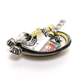 Quimper Ceramic Butter Dish: A Quimper ceramic butter dish. Featured is an oval dish, with a matching butter knife. Both pieces display a red floral center with a yellow and black border. The dish is marked to the verso with “Quimper C.P. F.56 D.110” and the knife blade is marked as stainless steel.