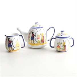 Hand-Painted Portuguese Ceramic Tea Set: A Portuguese ceramic tea set. This set includes a teapot, a creamer, and a sugar bowl. These pieces feature hand-painted figural and foliage scenes with blue trim. The underside of each is stamped “Hand Pained in Portugal”.
