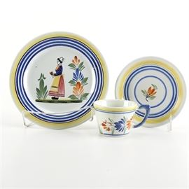 Henriot Quimper Faience Pieces: A selection of Henriot Quimper Faience pieces. This selection from Quimper is presented in the traditional Breton lady with yellow and blue bands. This selection includes a salad plate, saucer, and teacup. The pieces are marked on the underside.