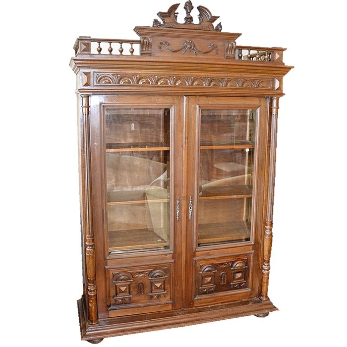 Victorian Style Knockdown China Cabinet: A Victorian style knockdown cabinet. This cabinet features an upper pediment with urn finial above a spindle surround to the top. Below are half fan carvings above two glass paneled doors that open to interior shelving. The cabinet doors are flanked by carved wood columns. The pieces rests on bun feet.